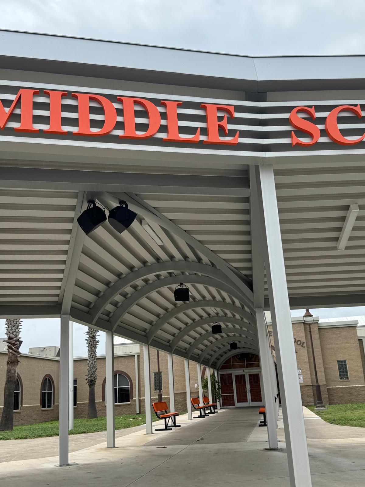 Pendant PA speakers under middle school entry canopy with orange lettering above