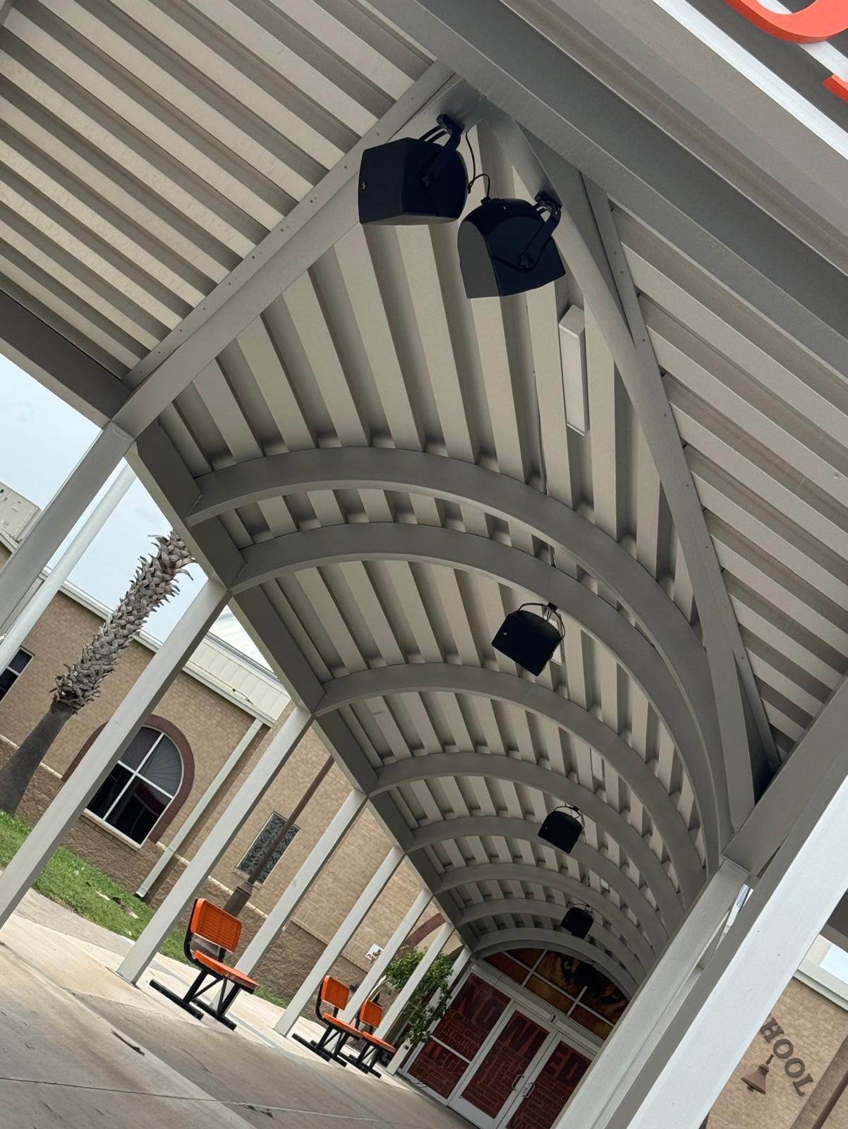 Overhead pendant PA speakers installed under a covered school walkway at a South Texas middle school